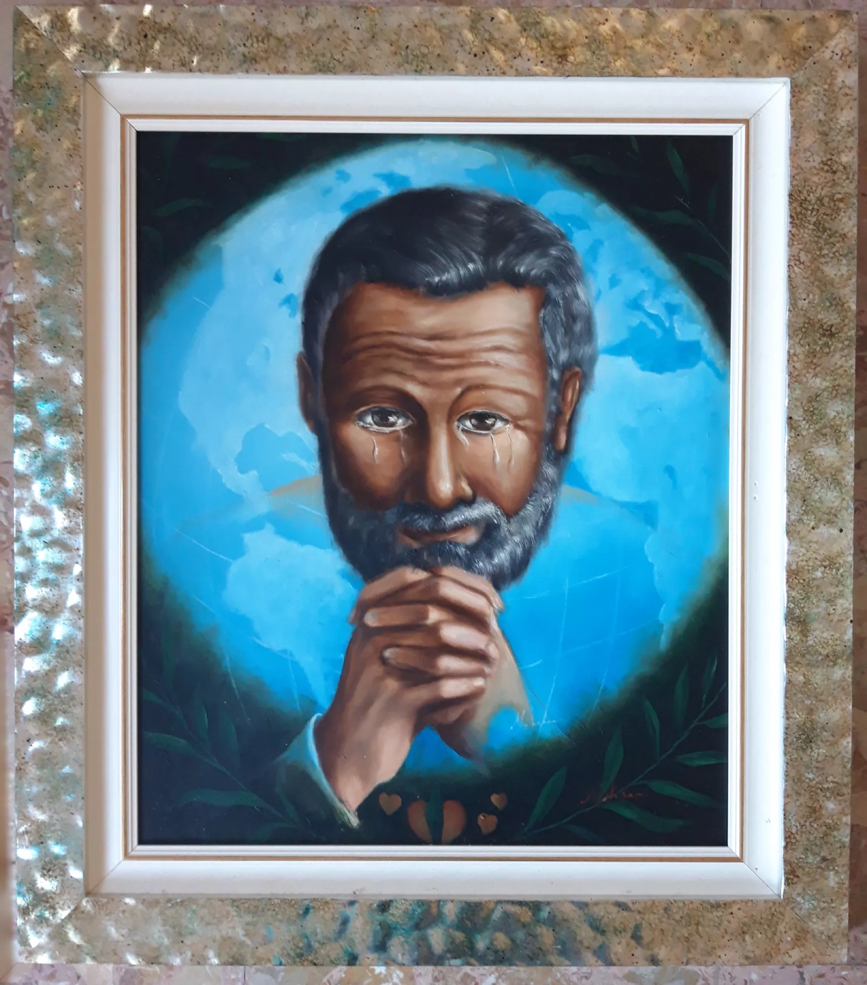 Dove-và-a-finire-il-mondo-Aly-Mohsen "Quadro di Ay Mohsen realizzato ad Olio con pennello. Il titolo è Dove và a finire il mondo e rientra nella categoria Il mondo di oggi. In Dove va a finire il mondo, Aly Mohsen realizza un autoritratto simbolico di forte intensità, trasformando il dolore personale in una riflessione universale sul destino dell’umanità. Il volto dell’artista, rigato di lacrime, e le mani giunte in un gesto di preghiera o invocazione introducono una dimensione di profonda introspezione spirituale, in cui la sofferenza individuale assume un valore collettivo. Alle spalle della figura emerge il pianeta Terra, raffigurato come una sfera azzurra sospesa nello spazio. Questo elemento assume una funzione simbolica centrale, evocando al tempo stesso fragilità, responsabilità condivisa e precarietà del futuro. Il dialogo visivo tra il primo piano umano e la dimensione planetaria costruisce una tensione tra intimità e universalità, tra esperienza personale e coscienza globale. La pittura, morbida e controllata, è dominata da tonalità di blu e verde che contribuiscono a creare un’atmosfera meditativa e silenziosa. Il linguaggio figurativo rimane saldo e leggibile, evitando effetti espressivi eccessivi in favore di una costruzione equilibrata e contemplativa dell’immagine. La cornice chiara, elegante e materica, dialoga con la composizione senza sovrapporsi al contenuto simbolico, valorizzando la profondità cromatica e rafforzando l’unità visiva dell’opera. Inserita nel contesto del realismo simbolico contemporaneo, Dove va a finire il mondo si configura come uno dei lavori più intimi e riflessivi di Aly Mohsen, in cui l’autoritratto diventa strumento di interrogazione etica e spirituale sul presente e sul futuro dell’umanità."