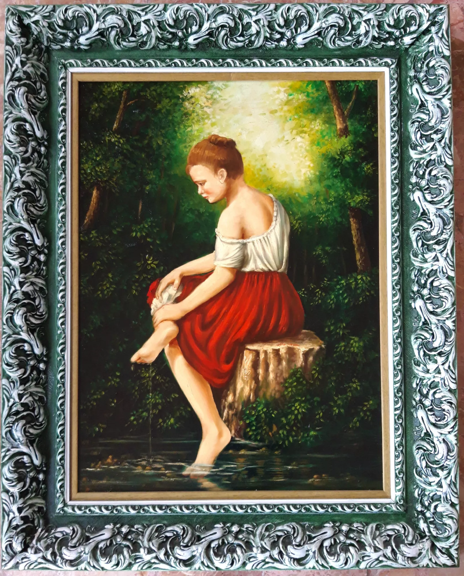 Donna-al-fiume-Aly-Mohsen "Quadro di Ay Mohsen realizzato ad Olio con pennello. Il titolo è Donna al fiume e rientra nella categoria C'era una volta. In Donna al fiume, Aly Mohsen sviluppa una scena figurativa di grande equilibrio e intimità, incentrata sul rapporto silenzioso tra figura femminile e ambiente naturale. La giovane donna, seduta lungo la riva, immerge i piedi nell’acqua in un gesto semplice e quotidiano, trasformato dall’artista in un momento di raccoglimento e introspezione. La composizione è essenziale e misurata: la postura raccolta e lo sguardo rivolto verso il basso suggeriscono una dimensione interiore, mentre il paesaggio fluviale avvolge la figura senza dominarla. La luce filtrata tra la vegetazione crea un’atmosfera morbida e contemplativa, accentuando il contrasto cromatico tra i verdi profondi dello sfondo e il rosso caldo della gonna, fulcro visivo della scena. L’acqua del fiume assume un valore simbolico di passaggio, purificazione e continuità, elementi ricorrenti nella ricerca figurativa di Mohsen. La resa pittorica è controllata e sensibile, attenta ai riflessi, ai tessuti e al fogliame, con una figurazione realista priva di idealizzazioni e concentrata sulla naturalezza del gesto. L’opera è completata da una cornice originale finemente lavorata, ricca ma armoniosa, che conferisce al dipinto una presenza espositiva di carattere museale e rafforza il dialogo tra eleganza formale e semplicità del soggetto."