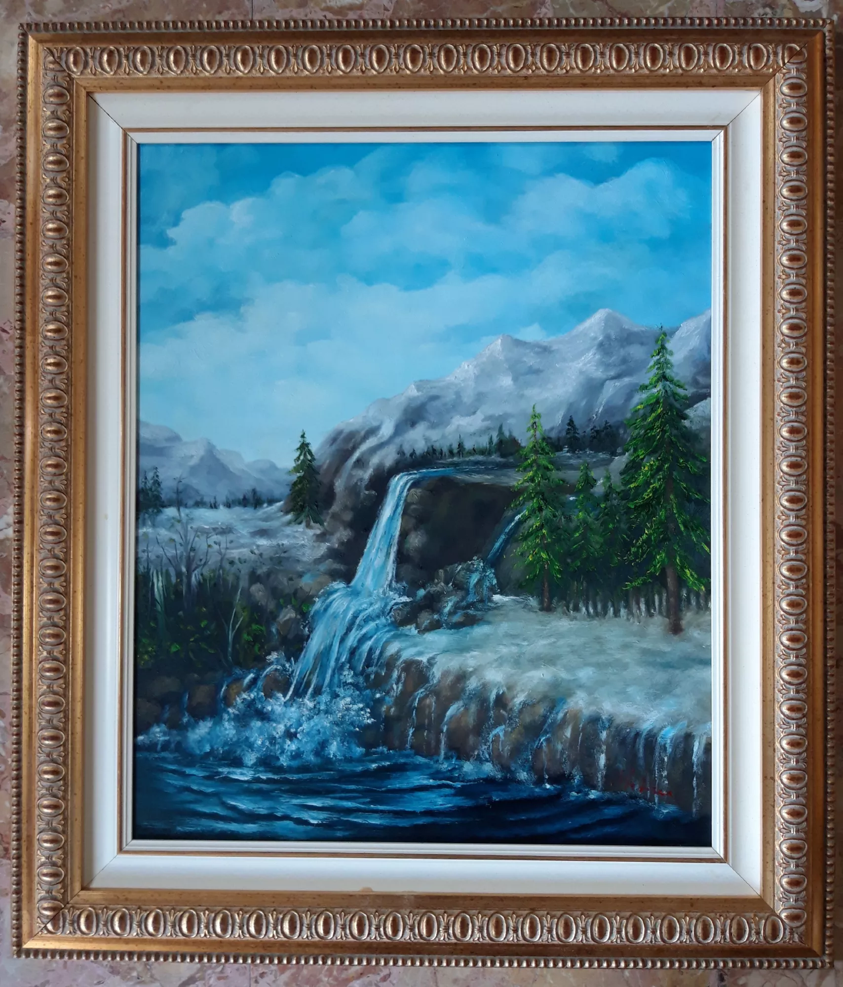 La-cascata-Aly-Mohsen "Quadro di Ay Mohsen realizzato ad Olio con pennello. Il titolo è La cascata e rientra nella categoria Paesaggi. La cascata è un dipinto figurativo di Aly Mohsen dedicato alla forza, alla purezza e alla continuità della natura montana. La composizione si struttura attorno al fluire dell’acqua che scende dalla roccia e accompagna lo sguardo verso il bacino sottostante, creando un equilibrio dinamico tra movimento e stabilità. Il paesaggio è costruito attraverso un attento dialogo cromatico tra l’azzurro del cielo, i verdi intensi degli abeti e i toni freddi della roccia, elementi che concorrono a definire una profondità spaziale chiara e una forte coerenza visiva. L’acqua, resa con particolare attenzione luministica, diventa il fulcro narrativo dell’opera, simbolo di energia vitale e di continuità naturale. La pennellata è controllata e descrittiva, capace di restituire la solidità delle masse rocciose e, al tempo stesso, la fluidità del corso d’acqua. Il contrasto tra le superfici ferme e il movimento della cascata conferisce alla scena una tensione equilibrata, mai drammatica, orientata piuttosto a una lettura contemplativa del paesaggio. L’atmosfera complessiva è limpida e ariosa, priva di elementi accessori, e invita l’osservatore a soffermarsi sul rapporto essenziale tra acqua, roccia e vegetazione. In questo senso, l’opera si colloca nella tradizione del paesaggio figurativo come spazio di armonia e osservazione silenziosa della natura. La cornice classica dorata, riccamente lavorata, valorizza il dipinto, ne rafforza il carattere decorativo e accompagna la composizione con eleganza e solidità formale. La cascata si inserisce nella produzione paesaggistica di Aly Mohsen come un’opera di equilibrio compositivo e chiarezza narrativa, capace di unire resa naturalistica, sensibilità luministica e una visione coerente della natura montana."