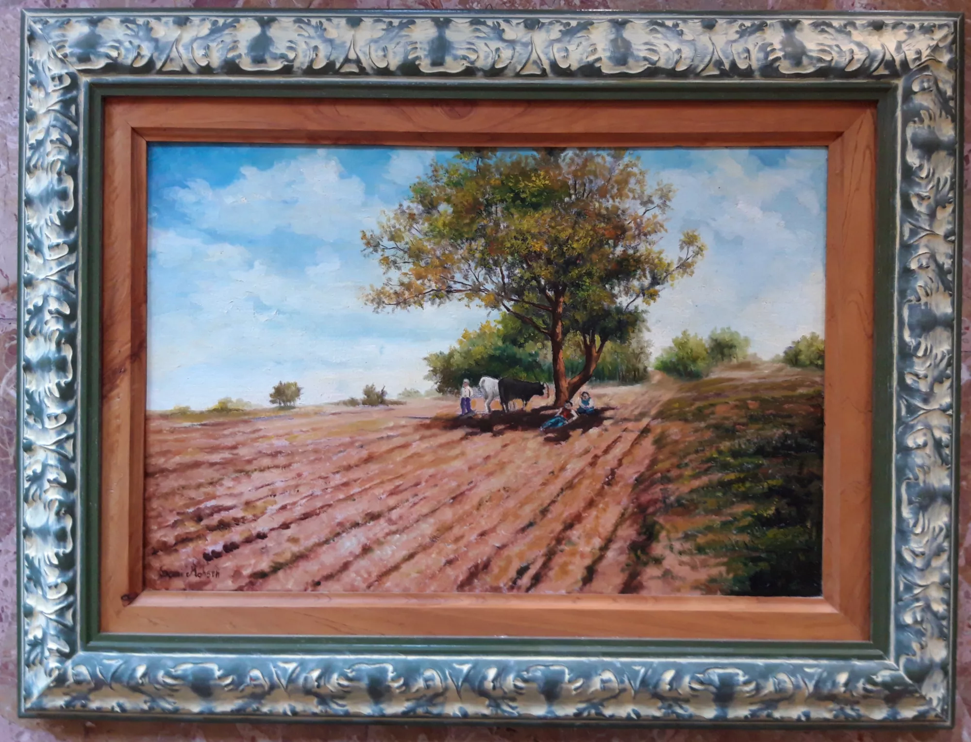 Campo-arato-Aly-Mohsen "Quadro di Ay Mohsen realizzato ad Olio con pennello. Il titolo è Campo arato e rientra nella categoria Paesaggi. Campo arato è un dipinto figurativo di Aly Mohsen che rappresenta un paesaggio rurale essenziale e autentico, incentrato sul rapporto diretto tra uomo, terra e cicli naturali. Un ampio campo arato si apre verso l’orizzonte, scandito da solchi regolari che guidano lo sguardo in profondità e costruiscono una solida struttura prospettica. Al centro della composizione, un grande albero domina la scena offrendo ombra e riparo. Sotto la sua chioma si raccoglie una semplice scena di vita contadina, discreta e misurata, che introduce una presenza umana silenziosa e rafforza il senso di equilibrio e quotidianità dell’opera. La figura umana non interrompe il paesaggio, ma vi si integra con naturalezza, diventandone parte integrante. La tavolozza cromatica è calda e naturale: i toni bruni e rossastri della terra dialogano con i verdi della vegetazione e con l’azzurro luminoso del cielo, creando un’atmosfera pacata e armoniosa. La luce è diffusa e stabile, priva di effetti drammatici, e contribuisce a restituire una percezione di tempo lento e continuo. La pennellata è sicura e descrittiva, capace di rendere la matericità del terreno arato, la compattezza dell’albero e la leggerezza dell’aria. L’equilibrio tra costruzione formale e sensibilità narrativa colloca l’opera all’interno della tradizione del paesaggio figurativo classico, reinterpretata con linguaggio sobrio e contemporaneo. La cornice, scelta con attenzione, riprende i toni del cielo e della terra, integrandosi armoniosamente con il dipinto e valorizzandone l’unità cromatica e compositiva. Campo arato si inserisce nella produzione paesaggistica di Aly Mohsen come un’opera di chiarezza formale e coerenza espressiva, capace di trasmettere un senso di stabilità, lavoro e continuità tra l’uomo e il paesaggio rurale."