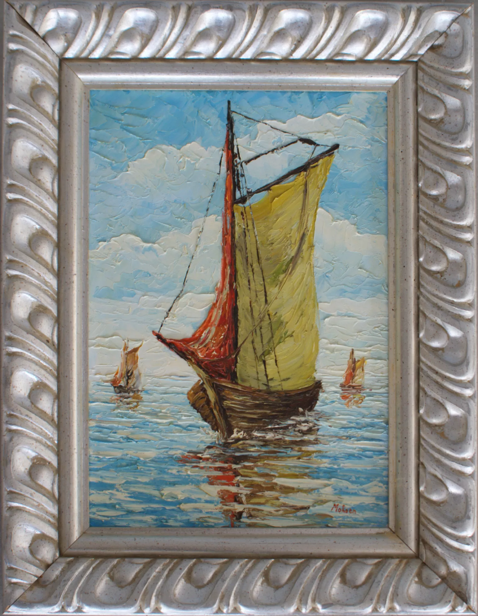 Boat-with-two-small-boats-in-the-background-Aly-Mohsen "Painting by Aly Mohsen, executed in Oil on canvas (palette knife). The title is Boat with two small boats in the background and it belongs to the category The Sea. Boat with two small boats in the background is an original painting by Aly Mohsen depicting a traditional sailboat in the foreground, advancing slowly across calm waters, with two smaller boats in the distance that expand the spatial depth of the scene and reinforce a clear sense of perspective. The work is executed in oil on canvas using a palette-knife technique, a central aspect of the artist’s pictorial approach, which gives the surface pronounced material texture and vivid luminous intensity. The composition is defined by the chromatic dialogue between the yellow-ochre sail and the lateral red sail, which stand out against the blues and light blues of the sea and sky. Energetic, layered palette-knife strokes shape a living, reflective sea, where the boat’s reflection creates dynamic effects of light and movement. The sky, also worked with a palette knife, features soft yet animated clouds that contribute to an atmosphere that is both serene and visually engaging. The subject, simple yet powerful, evokes universal themes such as journey, freedom, and Mediterranean maritime tradition—recurring elements in Aly Mohsen’s figurative production. The inclusion of the boats in the background adds compositional balance and a subtle narrative dimension that enhances the overall visual coherence of the painting. The work is completed by a finely crafted silver-toned frame with classical relief motifs, enclosing the composition with elegance and solidity while enhancing the luminosity of the colors and the expressive strength of the painted surface."