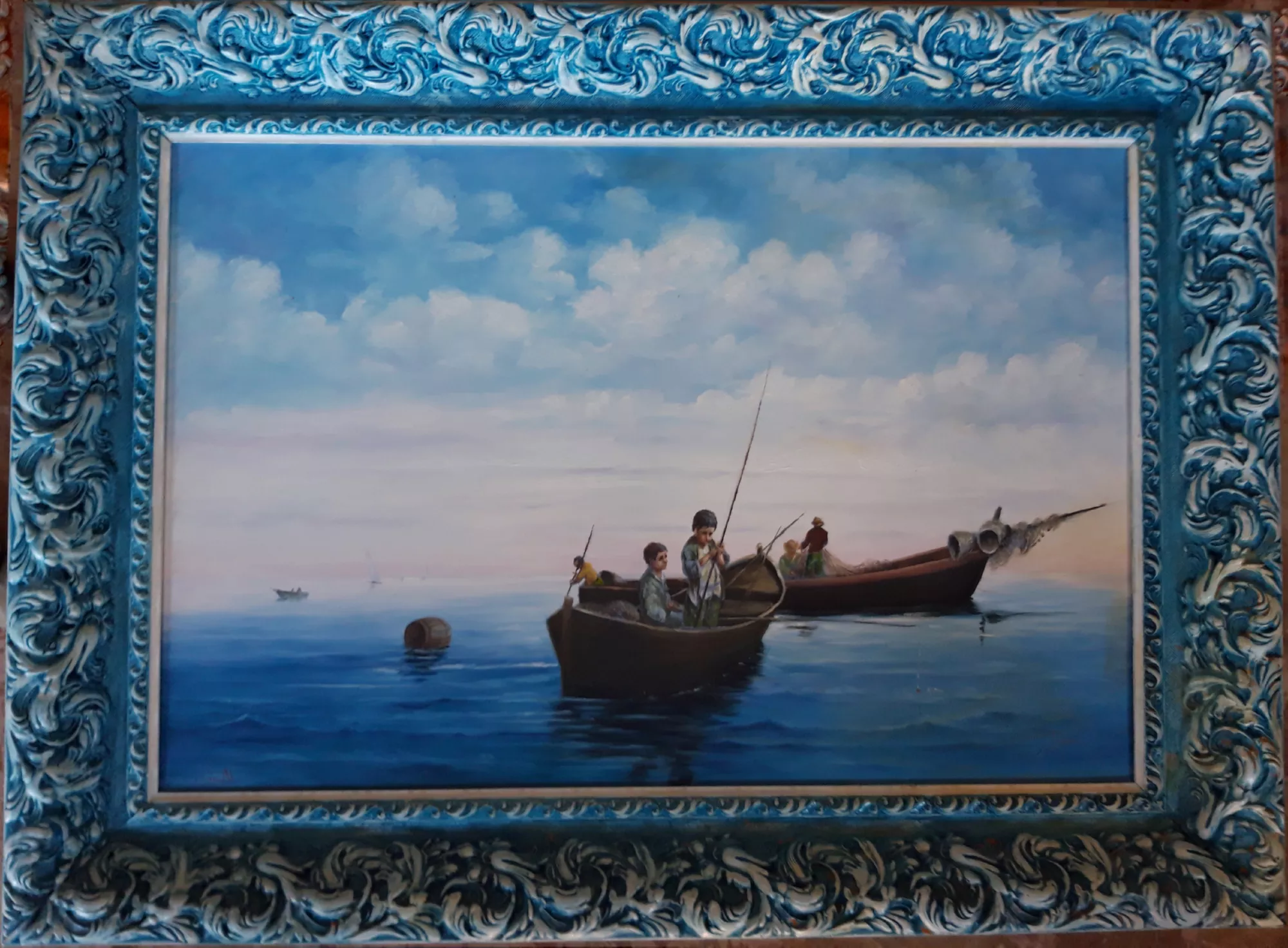 Piccoli-pescatori-in-barca-Aly-Mohsen "Quadro di Ay Mohsen realizzato ad Olio con pennello. Il titolo è Piccoli pescatori in barca e rientra nella categoria Il mare. Opera originale di Aly Mohsen che raffigura una scena di piccoli pescatori in barca, ambientata in un paesaggio marino di grande quiete e delicatezza narrativa. Il dipinto rappresenta due imbarcazioni tradizionali con giovani pescatori intenti alla pesca, colti in un momento di sospensione e silenzio, riconducibile alle ore iniziali o finali della giornata lungo la costa della Riviera ligure. La composizione è impostata con equilibrio e chiarezza spaziale: le barche si collocano in primo piano emergendo con naturalezza dalla superficie dell’acqua, resa attraverso passaggi cromatici morbidi e graduali che riflettono il cielo e contribuiscono a un senso diffuso di calma. Le figure, descritte con misura e sobrietà, introducono una dimensione umana discreta, richiamando temi universali legati al lavoro quotidiano e al rapporto diretto tra uomo e mare. Il mare occupa una parte significativa della scena ed è dipinto con tonalità di blu profondi e sfumature più chiare, modulati per suggerire un movimento lento e continuo. I riflessi sull’acqua stabiliscono un dialogo visivo con il cielo, rafforzando la coerenza luminosa e l’unità atmosferica dell’opera. Il cielo, ampio e luminoso, è costruito con toni delicati e nuvole leggere che ampliano la profondità visiva e accentuano il carattere contemplativo del dipinto. L’orizzonte basso contribuisce a una percezione di spazio aperto e silenzioso, mentre la resa pittorica, attenta ma mai descrittiva in modo rigido, evidenzia la maturità tecnica e narrativa di Aly Mohsen. L’opera è completata da una cornice decorativa finemente lavorata, caratterizzata da motivi classici e da una patinatura nei toni dell’azzurro e del bianco che richiama cromaticamente il mare e il cielo della composizione. La cornice si integra armoniosamente con il dipinto, contribuendo a definirne l’eleganza formale e l’unità visiva complessiva."