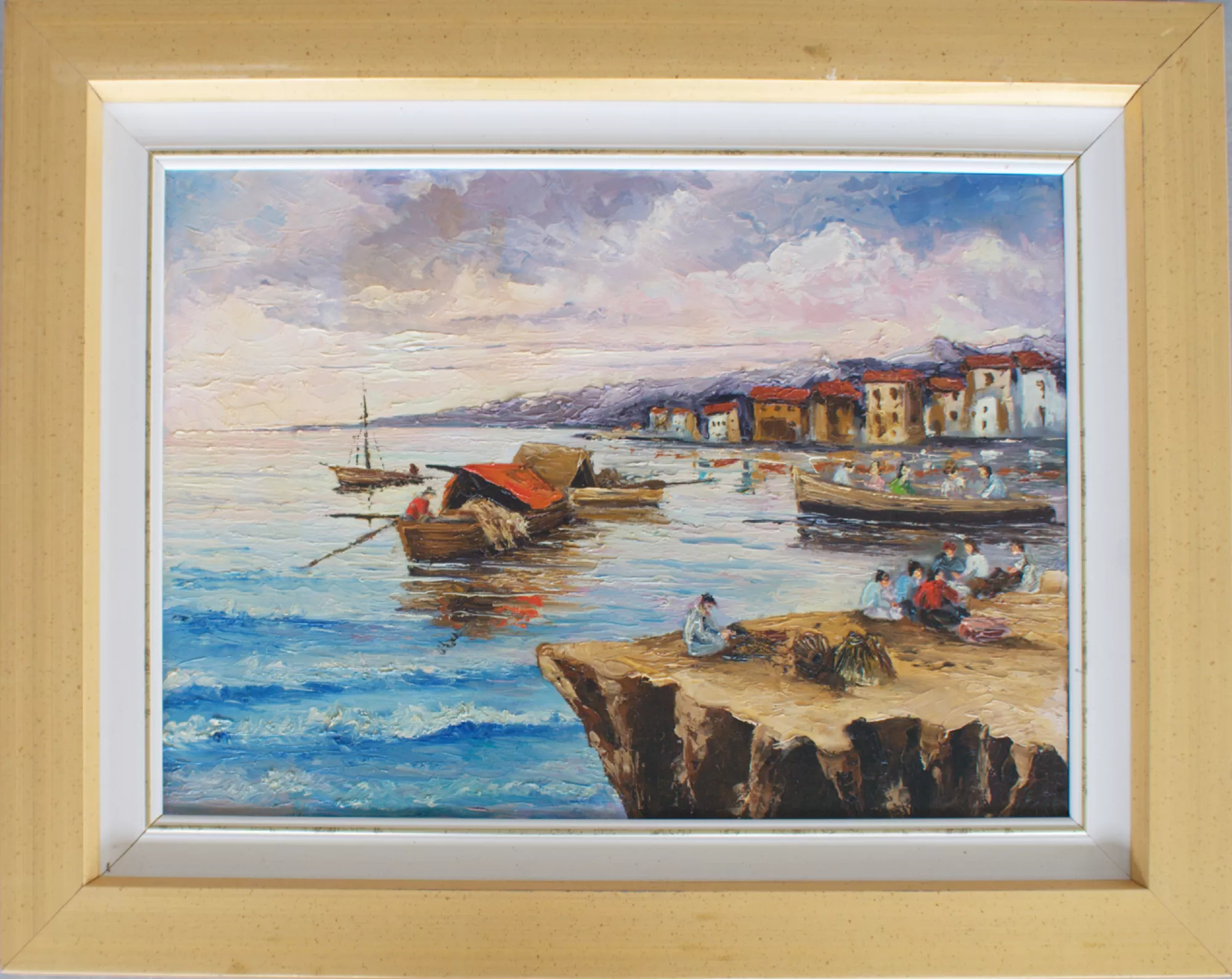 Fishermen’s-Village-Aly-Mohsen "Painting by Aly Mohsen, executed in Oil on canvas (palette knife). The title is Fishermen’s Village and it belongs to the category The Sea. Original work by Aly Mohsen depicting a fishermen’s village overlooking the sea, interpreted through a palette knife technique that gives the pictorial surface a strong material presence and pronounced visual intensity. The subject belongs to the artist’s Mediterranean seascape production, in which the coastal landscape becomes a setting for everyday life, memory, and the enduring relationship between humankind and the sea. In the foreground, a rocky shoreline unfolds, shaped through decisive palette-knife applications that form compact, irregular reliefs. Several figures are positioned within this space, engaged in daily activities and rendered in a simplified yet expressive manner, conveying a sense of community and continuity with maritime tradition. The arrangement of figures and painted masses naturally guides the viewer’s gaze toward the water, structuring the composition with balance and rhythmic movement. The sea occupies a central role in the painting and is rendered through layered applications of color applied with energy, capturing movement and the reflection of light across the surface. Fishing boats, either stationary or gently rocking, are mirrored in the water through subtle chromatic vibrations that enrich the spatial depth. In the background, the coastal village—composed of compact buildings in warm tones—integrates harmoniously into the landscape, evoking a Mediterranean setting closely associated with the Ligurian Riviera. The wide and luminous sky is built through soft yet textured chromatic transitions, suggesting a moment of the day suspended between morning and afternoon. The palette knife allows Aly Mohsen to synthesize volumes and perspective while maintaining spatial clarity, demonstrating technical and stylistic maturity. The painting is completed by a gold-toned frame with a lighter inner border, which encloses the composition in a balanced manner and enhances its chromatic range, giving the artwork a coherent and resolved visual presence."