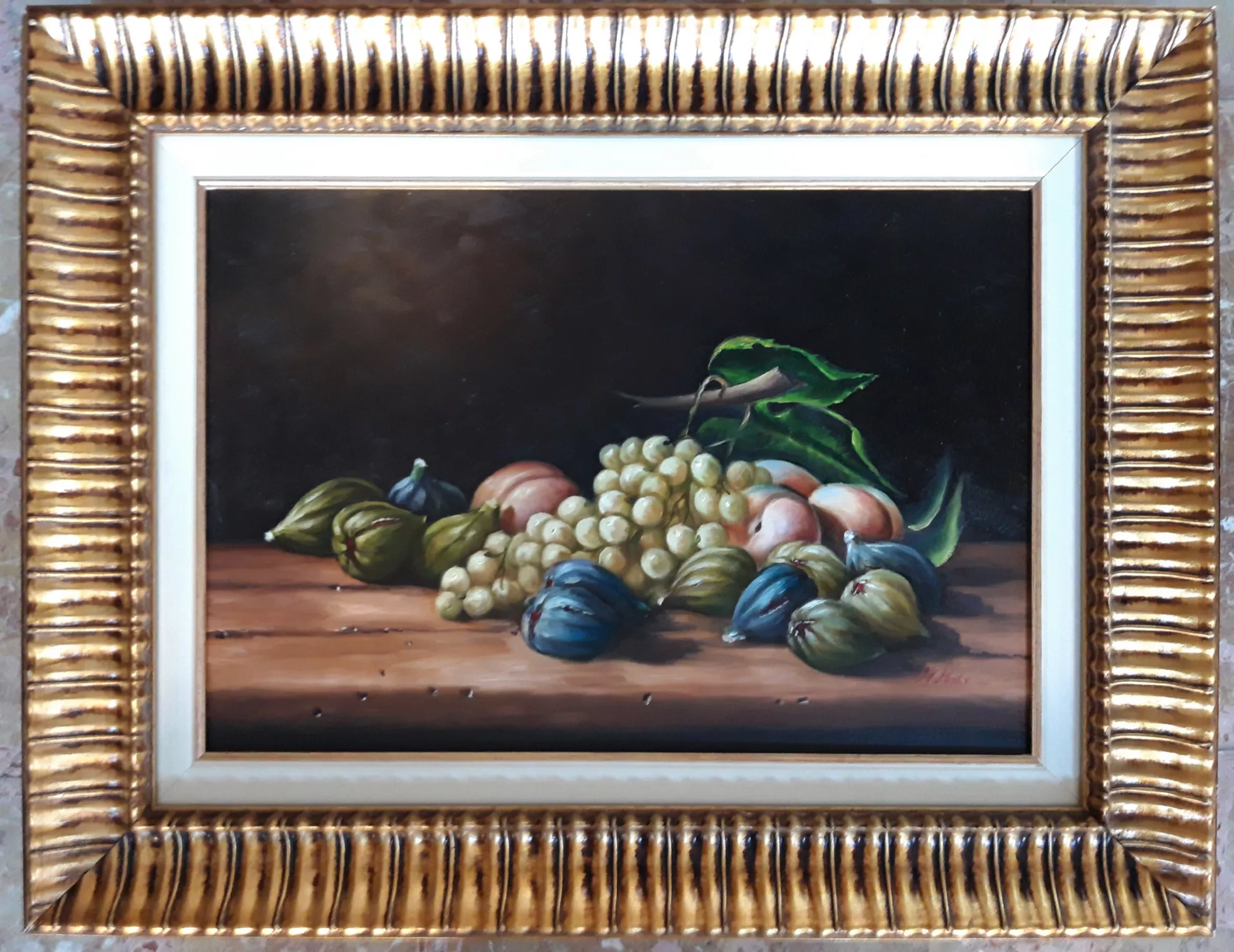 Natura-morta-con-fichi-e-uva-Aly-Mohsen "Quadro di Ay Mohsen realizzato ad Olio con pennello. Il titolo è Natura morta con fichi ed uva e rientra nella categoria Natura morta. Opera originale di Aly Mohsen che raffigura una natura morta di impianto classico, inserita nel filone della pittura figurativa e caratterizzata da un’attenta ricerca formale e luministica. La composizione presenta un gruppo di uva bianca, fichi maturi e pesche disposti su un piano ligneo, collocati davanti a un fondo scuro che accentua la profondità spaziale e concentra l’attenzione sull’equilibrio dei volumi. La resa pittorica è affidata a un uso controllato del pennello, con superfici morbide e passaggi tonali graduali. La luce, calibrata e diffusa, modella i frutti mettendo in evidenza le diverse qualità materiche: la trasparenza degli acini d’uva, la consistenza dei fichi, la compattezza delle pesche e la freschezza delle foglie. L’insieme restituisce un’immagine sospesa e silenziosa, in continuità con la tradizione della natura morta come esercizio di osservazione e misura. L’opera evidenzia la padronanza tecnica di Aly Mohsen nella pittura figurativa, unita a una sensibilità compositiva che privilegia l’armonia dell’insieme e la chiarezza della struttura visiva. La scelta del soggetto e la cura dei dettagli rimandano a una pratica pittorica fondata sullo studio della luce, del colore e delle relazioni tra gli elementi. Il dipinto è completato da una cornice in legno dorato, riccamente lavorata, con profilo interno chiaro che crea una separazione visiva ordinata tra l’opera e il bordo. La cornice contribuisce a rafforzare l’impostazione classica del dipinto e ne valorizza l’equilibrio cromatico complessivo. Opera firmata e unica."