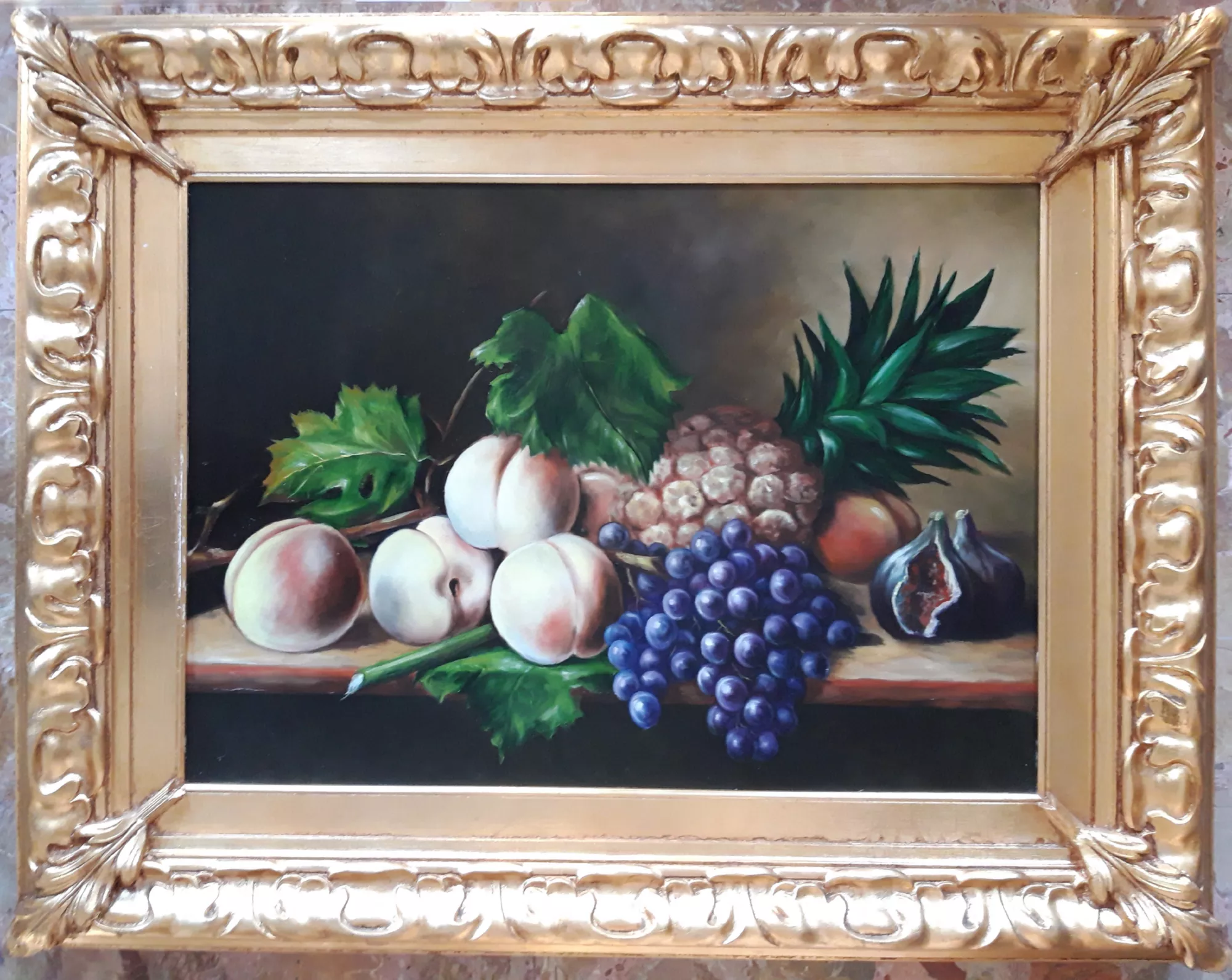 Natura-morta-con-ananas-pesche-uva-Aly-Mohsen "Quadro di Ay Mohsen realizzato ad Olio con pennello. Il titolo è Natura morta con ananas, pesche e uva e rientra nella categoria Natura morta. Opera originale di Aly Mohsen che raffigura una natura morta di impostazione classica, inserita nel contesto della pittura figurativa e caratterizzata da un attento equilibrio compositivo e luministico. La scena presenta un insieme di frutti — ananas, pesche, uva viola e fichi — disposti su un piano orizzontale secondo una struttura ordinata, che mette in relazione forme, volumi e cromie con misurata armonia. La resa pittorica è affidata a una tecnica a pennello precisa e controllata, attraverso la quale l’artista restituisce con chiarezza le diverse qualità materiche degli elementi rappresentati. La superficie dell’ananas, la morbidezza vellutata delle pesche, la trasparenza degli acini d’uva e il contrasto interno del fico aperto sono trattati con attenzione analitica e sensibilità luminosa. Il fondo scuro, uniforme e profondo, isola la composizione e accentua il carattere silenzioso e contemplativo della natura morta. L’opera testimonia la padronanza tecnica di Aly Mohsen nel genere della natura morta, intesa come spazio di studio della luce, del colore e delle relazioni tra gli oggetti. La composizione, priva di elementi narrativi accessori, privilegia la stabilità formale e la chiarezza visiva, in continuità con la tradizione pittorica classica reinterpretata in chiave personale. Il dipinto è completato da una cornice in legno dorato finemente lavorata, con decorazioni classiche in rilievo. Il profilo interno chiaro crea una separazione visiva netta tra opera e bordo, contribuendo a valorizzare l’equilibrio cromatico e l’impostazione museale dell’insieme. Opera firmata e unica."