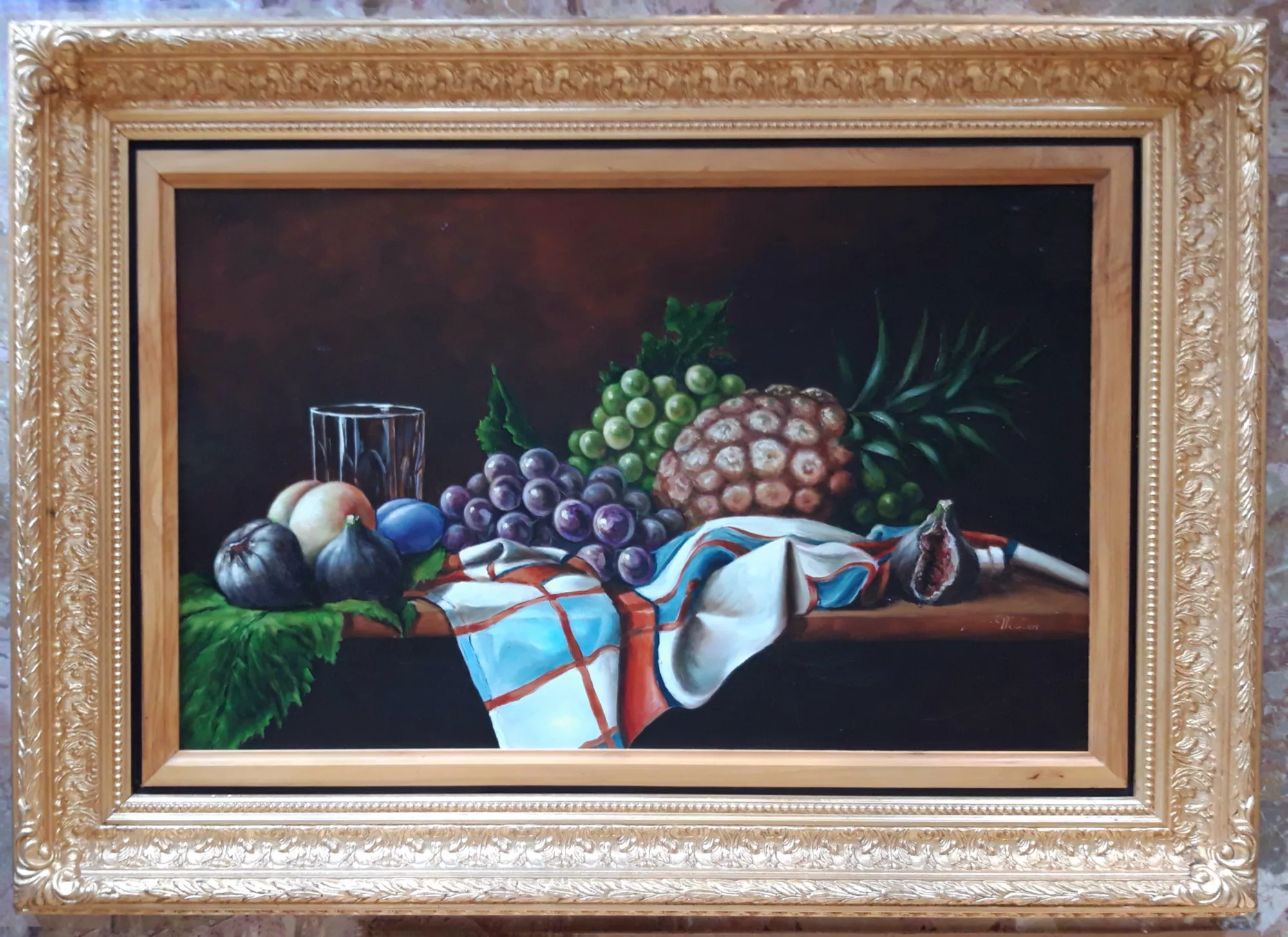 Natura-morta-con-frutta-su-canovaccio-Aly-Mohsen "Quadro di Ay Mohsen realizzato ad Olio con pennello. Il titolo è Natura morta con frutta su canovaccio e rientra nella categoria Natura morta. Opera originale di Aly Mohsen appartenente alla sua produzione di natura morta figurativa, nella quale il genere classico viene affrontato con rigore compositivo e attenzione analitica alla luce e alla materia. La composizione presenta un insieme di frutti maturi — uva, ananas, fichi e pesche — disposti su un piano ligneo e accompagnati da un bicchiere in vetro e da un canovaccio drappeggiato, elementi che introducono una dimensione domestica e quotidiana alla scena. La pittura è eseguita a pennello con tecnica accurata e controllata, finalizzata alla restituzione precisa dei volumi e delle diverse qualità superficiali. La trasparenza del vetro, la consistenza compatta dell’ananas, la morbidezza del tessuto e la luminosità degli acini d’uva sono trattate con sensibilità luministica e attenzione al dettaglio. Il fondo scuro, uniforme e profondo, richiama la tradizione della natura morta classica e contribuisce a isolare gli oggetti, rafforzandone la presenza plastica e la stabilità formale. L’opera si inserisce nel percorso di Aly Mohsen come studio equilibrato del rapporto tra luce, colore e forma, privilegiando una composizione stabile e misurata. L’assenza di elementi narrativi accessori concentra l’osservazione sulla relazione tra gli oggetti e sul valore pittorico della loro resa, in continuità con la tradizione della pittura figurativa. Il dipinto è completato da una cornice in legno dorato finemente decorata, di gusto classico. Il profilo interno più sobrio crea una separazione visiva ordinata tra l’immagine e il bordo, valorizzando l’equilibrio cromatico e conferendo all’opera un’impostazione museale. Opera firmata e unica."