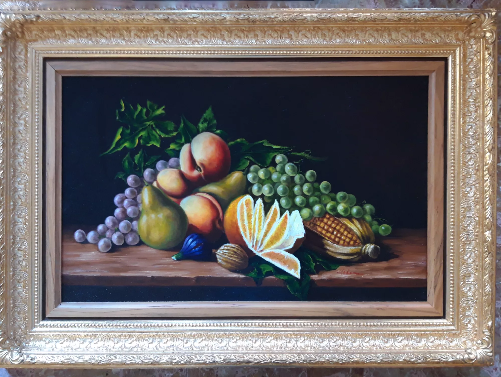 Natura-morta-con-uva-pannocchia-arancia-Aly-Mohsen "Quadro di Ay Mohsen realizzato ad Olio con pennello. Il titolo è Natura morta con uva, pannocchia ed arancia e rientra nella categoria Natura morta. Opera originale di Aly Mohsen, appartenente alla sua produzione di natura morta figurativa, nella quale il genere classico viene affrontato con attenzione analitica alla luce, alla composizione e alla resa delle superfici. Il dipinto raffigura un assortimento di frutti — uva chiara e violacea, pere, pesche, un’arancia aperta e una pannocchia — disposti su un piano ligneo secondo un equilibrio formale misurato e stabile. La luce, proveniente lateralmente, modella con gradualità i volumi e definisce le diverse qualità materiche: la trasparenza degli acini d’uva, la consistenza vellutata delle pesche, la polpa luminosa dell’arancia e la struttura compatta della pannocchia. La pittura è eseguita a pennello con controllo e precisione, privilegiando passaggi tonali morbidi e una costruzione chiara delle forme. Il fondo scuro, uniforme e privo di elementi accessori, isola gli oggetti e rafforza il carattere contemplativo della scena. L’opera si colloca nel percorso di Aly Mohsen come esercizio di sintesi tra tradizione della natura morta e sensibilità figurativa contemporanea. L’attenzione è concentrata sulla relazione tra luce e materia, senza intenti narrativi, in una composizione che valorizza stabilità, silenzio visivo e chiarezza strutturale. Il dipinto è completato da una cornice ampia in legno dorato finemente decorata, di gusto classico. Il profilo interno più sobrio crea una separazione visiva ordinata tra immagine e bordo, contribuendo a un’impostazione complessiva di carattere museale. Opera firmata e unica."
