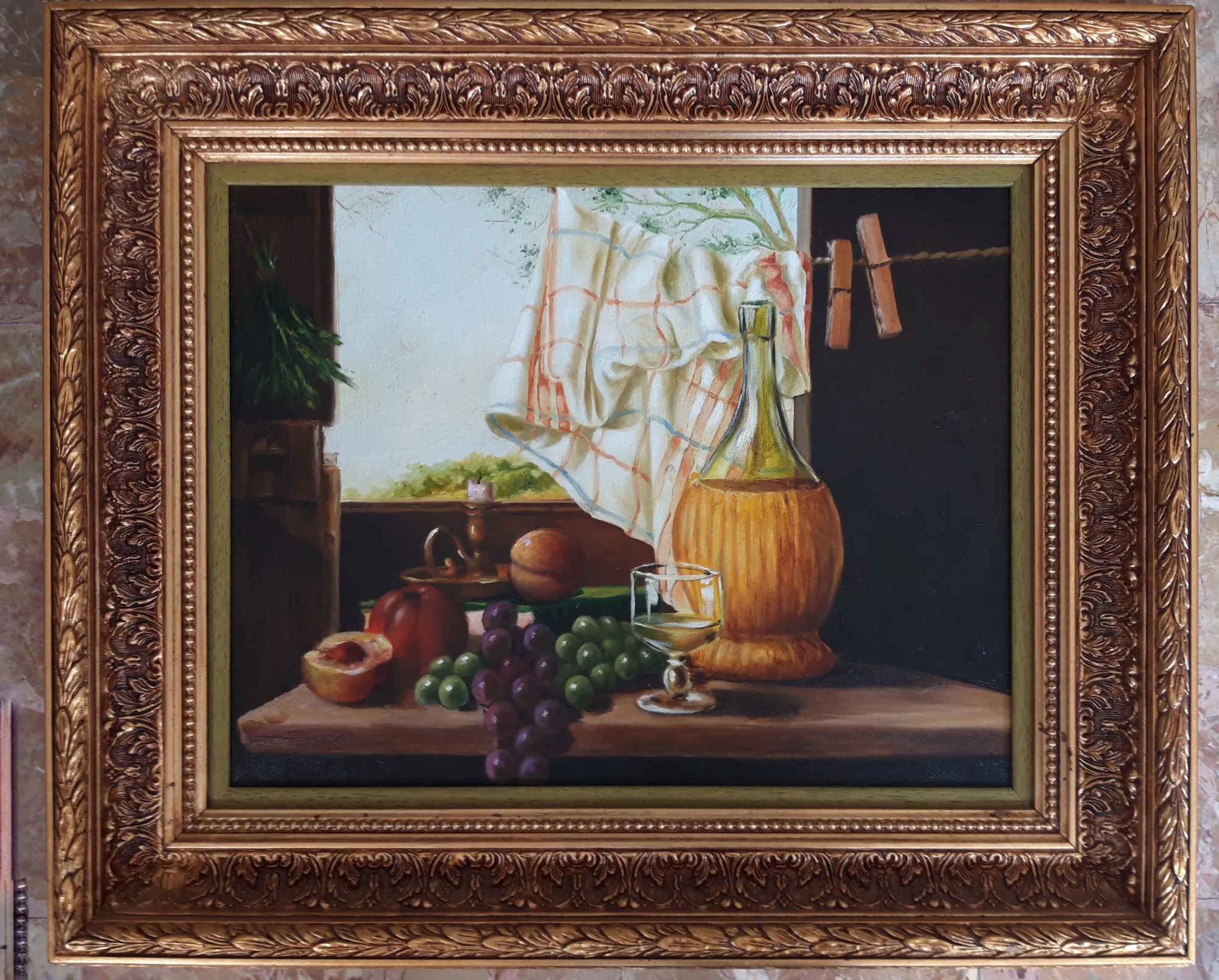 Still-life-with-flask,-candle,-and-window-view-Aly-Mohsen "Painting by Aly Mohsen, executed in Oil on canvas (brush). The title is Still life with flask, candle, and window view and it belongs to the category Still Life. Original work by Aly Mohsen, this figurative still life brings together the classical painting tradition with a carefully structured and balanced composition. In the foreground, arranged on a wooden surface, are an amber glass flask, a transparent drinking glass, clusters of light and dark grapes, ripe peaches, and opened fruit, all rendered with close attention to volume, surface texture, and the behavior of light. The scene is organized around a dialogue between interior and exterior space: an open window in the background introduces a subtle natural view and diffused light that enters the interior, softening contrasts and expanding visual depth. A light-colored cloth, held in place with clothespins and shaped by natural folds, adds a sense of movement that balances the stillness of the objects and gently directs the viewer’s gaze toward the center of the composition. Executed entirely with the brush, the painting demonstrates precise and controlled technique, emphasizing the transparency of glass, the material qualities of the fruit, and the chiaroscuro relationship between the objects and the dark background. Careful attention to light and spatial arrangement gives the work a contemplative character, in which everyday elements are transformed into a quiet, formally resolved image. The artwork is completed by a wide, richly carved gilded wooden frame of classical design. The more restrained inner profile provides an ordered visual separation between image and frame, reinforcing the museum-like presentation and the formal coherence of the work."