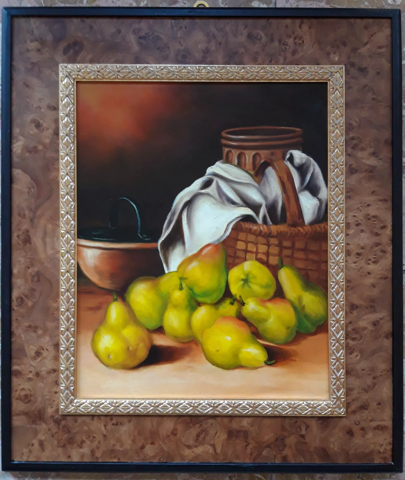 Still-life-with-pears-Aly-Mohsen "Painting by Aly Mohsen, executed in Oil on canvas (brush). The title is Still life with pears and it belongs to the category Still Life. Original work by Aly Mohsen, this figurative still life is distinguished by its balanced composition and restrained luminous intensity, characteristic of the artist’s mature production. In the foreground, a group of pears in golden and green tones is arranged on a warm, light-filled surface, organized in a natural disposition that emphasizes the diversity of forms and textures. The fruit is rendered with careful attention to material presence and light, through a precise and controlled brush technique that conveys the softness of the skins, subtle chromatic variations, and the full volumetric quality of the elements. In the background, a woven basket with a softly draped white cloth, a terracotta vessel, and a bowl extend the scene, establishing a clear dialogue with the classical still life tradition. The dark, gradually nuanced background isolates the subjects and enhances their three-dimensional presence, encouraging a focused and contemplative reading of the composition. The arrangement of elements follows a stable and measured structure, in which each object retains formal autonomy while contributing to a cohesive visual balance. The painting is completed by an articulated frame featuring a wide outer band with a dark burl-wood effect and a finely worked inner profile in lighter tones. The frame surrounds the artwork with clarity and restraint, reinforcing its formal presence and providing a coherent, museum-style presentation."