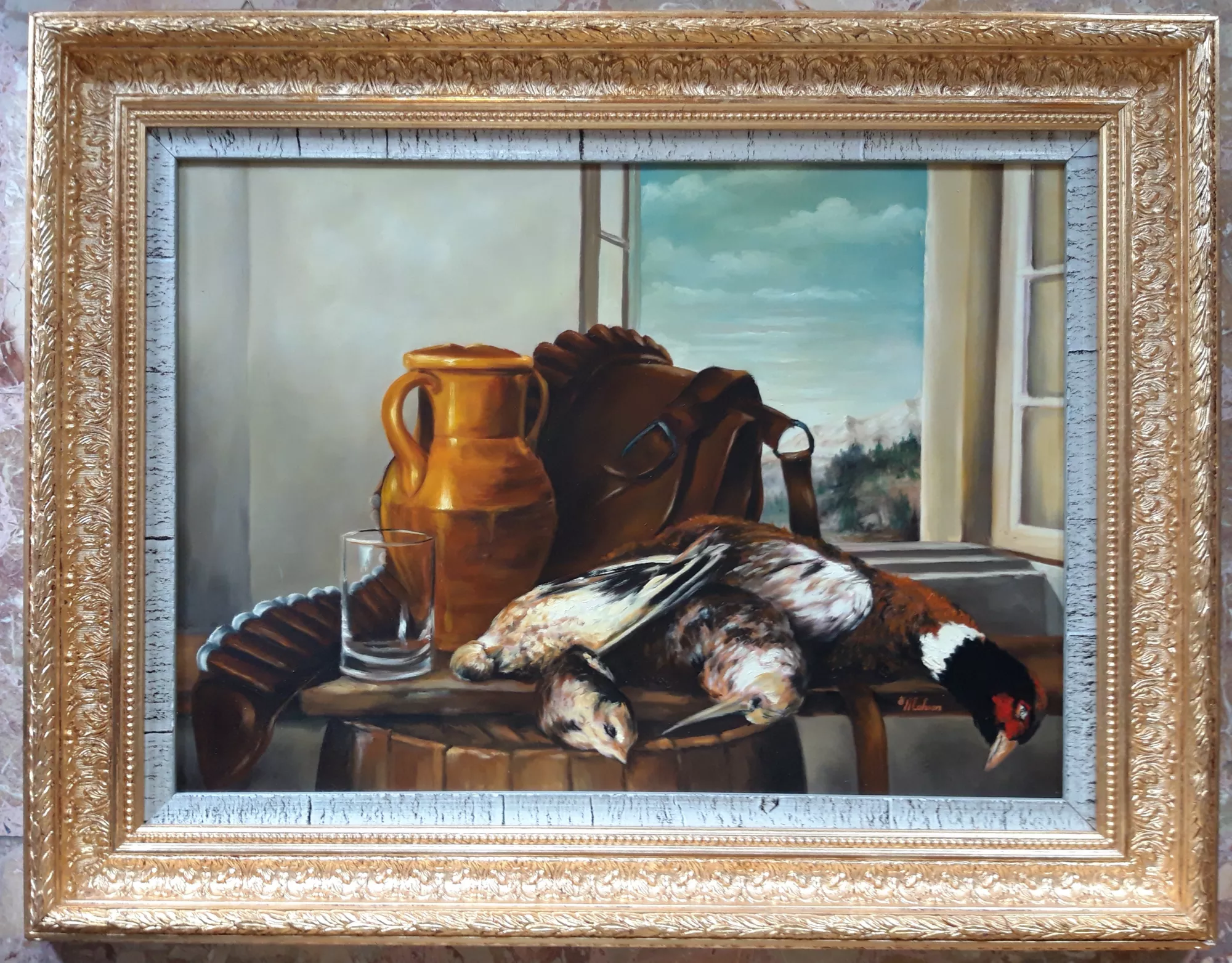 La-caccia-Aly-Mohsen "Quadro di Ay Mohsen realizzato ad Olio con pennello. Il titolo è La caccia e rientra nella categoria Natura morta. La caccia di Aly Mohsen è una natura morta figurativa di forte valore simbolico, concepita come opera gemella di La pesca, con la quale instaura un dialogo coerente sul tema ancestrale del rapporto tra l’uomo e la natura. L’artista affronta il soggetto venatorio non come rappresentazione di violenza, ma come gesto primario legato alla sopravvivenza, all’equilibrio e al rispetto del ciclo naturale della vita, in continuità concettuale con l’opera in coppia. In primo piano sono disposti quattro volatili da caccia — una quaglia, una pernice, una beccaccia e un fagiano — raffigurati con accurata attenzione anatomica e sensibilità pittorica. I corpi, adagiati su un piano ligneo, sono affiancati da oggetti funzionali alla scena: un fiasco in terracotta, un bicchiere di vetro trasparente e una borsa da caccia, elementi che rimandano a un contesto rurale essenziale, fatto di silenzio, gesti misurati e tradizioni consolidate. La composizione è arricchita dalla presenza di una finestra aperta sul paesaggio, che introduce luce naturale e profondità visiva, creando un equilibrio tra spazio interno ed esterno. La luce laterale, morbida e controllata, modella i volumi con gradualità, valorizzando la resa materica delle piume, della ceramica e delle superfici lignee. La tavolozza, dominata da tonalità calde e terrose, rafforza il legame con la terra e stabilisce una chiara continuità cromatica e tematica con La pesca. La pittura, realizzata a pennello, evidenzia una solida padronanza tecnica e una sensibilità di impronta classica, orientata alla chiarezza formale e alla costruzione equilibrata dell’immagine. L’opera si configura come una natura morta di carattere meditativo, nella quale ogni elemento contribuisce a una lettura sobria e contemplativa. Il dipinto è completato da una cornice riccamente decorata e dorata, con battuta interna chiara dall’aspetto leggermente patinato, che incornicia l’opera con eleganza classica e ne rafforza la presentazione di carattere museale."