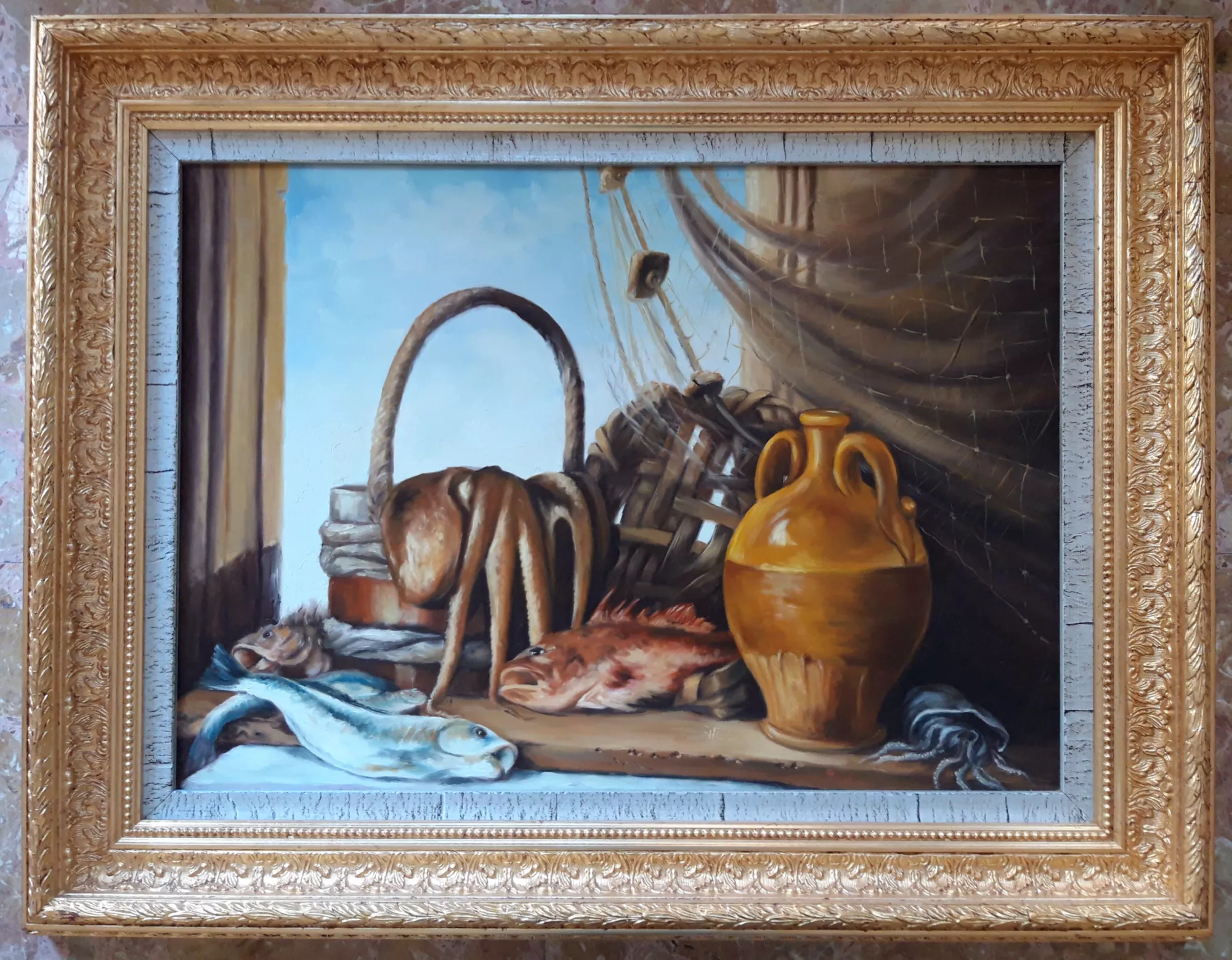 The-fishing-Aly-Mohsen "Painting by Aly Mohsen, executed in Oil on canvas (brush). The title is The fishing and it belongs to the category Still Life. The fishing by Aly Mohsen is a figurative still life of strong narrative intensity, conceived as the companion piece to The hunt, together forming a coherent diptych focused on the ancestral relationship between humankind and nature. Through the language of figurative painting, the artist interprets the return from fishing as a daily and ritual gesture, connected to work, survival, and respect for natural cycles, in direct conceptual dialogue with its paired work. The composition depicts an interior space opening toward the outside, where freshly caught fish are arranged on a wooden surface alongside the tools of the trade: a fishing net, a woven basket, a terracotta jug, a rope, and a transparent glass. The elements are organized with compositional balance and clarity, establishing a harmonious relationship between forms, materials, and textures. The open window introduces clear, airy natural light, expanding the visual space and creating a dialogue between interior and exterior. The painterly execution shows careful attention to material presence and realism: fish scales, glass transparency, ceramic porosity, and the woven texture of the net are rendered with precision and technical sensitivity. The chromatic palette, dominated by warm, natural tones, directly echoes that of The hunt, reinforcing the visual and thematic connection between the two paintings. Executed with the brush, the work demonstrates a solid command of the still-life tradition and a formal construction focused on balance and legibility. The painting presents itself as a contemplative scene, in which each element contributes to a restrained and measured narrative. The painting is completed by an important, richly decorated gilded frame with a light inner rebate featuring a subtly aged appearance, which surrounds the work with classical elegance and reinforces its museum-style presentation."