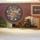 "Opera di Ay Mohsen realizzata con la tecnica dell'intarsio. Il titolo è Scrivania del poker e le tre carte e rientra nella categoria Ebanisteria Monumentale. Questa imponente scrivania monumentale rappresenta una delle opere più concettualmente audaci, raffinate e politicamente consapevoli di Aly Mohsen. In essa, la grande tradizione dell’ebanisteria artistica europea viene trasformata in strumento narrativo, simbolico e apertamente critico, dando vita a un’opera che trascende la funzione d’arredo per assumere la forma di messaggio cifrato e denuncia silenziosa. Non si tratta di un semplice mobile funzionale, ma di una vera opera d’arte tridimensionale, concepita per dialogare con il potere, smascherarne i meccanismi e mettere in crisi le apparenze di legalità e correttezza. Struttura e materiali La scrivania è caratterizzata da una struttura solida ma visivamente equilibrata, con gambe sagomate e slanciate che alleggeriscono la massa monumentale del piano. L’opera è realizzata con una selezione estremamente ricercata di legni pregiati, scelti non solo per le qualità estetiche ma anche per il loro valore simbolico: Noce nazionale e noce canaletto per la struttura principale e le superfici estese, apprezzati per la profondità cromatica e la stabilità nel tempo Radica di noce per i pannelli frontali, impiegata per ottenere superfici vibranti e irregolari, metafora visiva dell’instabilità e dell’inganno Ebano ed essenze scure tinte per i fondi degli intarsi, funzionali a rafforzare il contrasto grafico Acero e acero sicomoro per gli intarsi chiari Legni naturalmente colorati (padouk, acero, mogano, rovere, radica di noce, ebano verde ed ebano nero) per la resa cromatica delle figure e delle carte da gioco Il bordo chiaro e continuo del piano richiama deliberatamente la tradizione dei grandi tavoli da gioco, incorniciando la scena e convogliando lo sguardo verso il centro narrativo. Il piano: il gioco come metafora del potere Il piano superiore costituisce il cuore concettuale dell’opera. All’interno di una ricchissima cornice ornamentale intarsiata si sviluppa una sequenza di carte da poker disposte con apparente casualità. A una prima lettura, l’immagine suggerisce una partita in corso. A uno sguardo più attento, emerge però un elemento perturbante: le combinazioni non conducono a nessun esito logico. Le mani sono incoerenti, impossibili, volutamente manipolate. Questa ambiguità è intenzionale. Il poker, simbolo di strategia, calcolo e rischio controllato, viene qui messo in relazione con il gioco delle tre carte, archetipo universale della truffa. Il messaggio è sottile ma inequivocabile: chi crede di giocare secondo regole condivise è già vittima di un inganno. Il fronte: musica, scena e finzione Il fronte della scrivania è dominato da un grande medaglione circolare intarsiato, nel quale compaiono strumenti musicali, spartiti, carte da gioco e motivi floreali. La musica diventa metafora della messa in scena del potere: un concerto apparentemente armonioso che nasconde dissonanze profonde, una composizione elegante pensata per distrarre, sedurre e confondere. Le fasce laterali, ornate con ghirlande classiche e figure stilizzate, richiamano consapevolmente il linguaggio neoclassico e ottocentesco, rafforzando l’idea di ordine, autorità e rispettabilità — un ordine solo apparente. Storia dell’opera e valore simbolico La scrivania fu commissionata da un importante uomo d’affari egiziano, figura di enorme peso economico internazionale. Aly Mohsen, che conosceva il committente fin dall’infanzia, aveva fondati motivi per ritenere che questi operasse in realtà come prestanome per i servizi segreti statunitensi, coinvolto in operazioni economiche e finanziarie condotte in Italia. Al momento della consegna, Mohsen si recò personalmente nell’ufficio del committente e ne spiegò il significato con parole che rivelano la natura profonda dell’opera: «Questa scrivania serve per avvisare chi si siede di fronte a te: lui pensa di giocare a poker, mentre tu stai giocando al gioco delle tre carte.» Un’accusa di straordinaria eleganza, affidata non al linguaggio diretto ma alla forza simbolica dell’intarsio. Il committente, comprendendo perfettamente il messaggio, si sentì apertamente insultato e rifiutò l’opera. La scrivania rimase così nelle mani dell’artista. Rimasta nella disponibilità dell’artista, la Scrivania del Poker e del Gioco delle Tre Carte possiede oggi un valore ulteriormente accresciuto. È un pezzo unico, documentato, con una storia forte, verificabile e di straordinaria attrattiva per il collezionismo internazionale. L’opera unisce: alta ebanisteria artistica contenuto politico e narrativo qualità museale dimensioni monumentali provenienza diretta dall’artista Per collezionisti evoluti e investitori in mobili d’arte, arti decorative e opere concettuali, questa scrivania rappresenta un caso raro di arredo che diventa linguaggio critico, capace di dialogare con design, scultura e arte contemporanea, e destinato a una progressiva valorizzazione culturale e patrimoniale. In Aly Mohsen, il legno non è mai solo materia: diventa linguaggio, accusa, ironia e memoria. E questa scrivania ne è una delle dichiarazioni più lucide e implacabili."