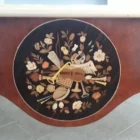 "Opera di Ay Mohsen realizzata con la tecnica dell'intarsio. Il titolo è Scrivania del poker e le tre carte e rientra nella categoria Ebanisteria Monumentale. Questa imponente scrivania monumentale rappresenta una delle opere più concettualmente audaci, raffinate e politicamente consapevoli di Aly Mohsen. In essa, la grande tradizione dell’ebanisteria artistica europea viene trasformata in strumento narrativo, simbolico e apertamente critico, dando vita a un’opera che trascende la funzione d’arredo per assumere la forma di messaggio cifrato e denuncia silenziosa. Non si tratta di un semplice mobile funzionale, ma di una vera opera d’arte tridimensionale, concepita per dialogare con il potere, smascherarne i meccanismi e mettere in crisi le apparenze di legalità e correttezza. Struttura e materiali La scrivania è caratterizzata da una struttura solida ma visivamente equilibrata, con gambe sagomate e slanciate che alleggeriscono la massa monumentale del piano. L’opera è realizzata con una selezione estremamente ricercata di legni pregiati, scelti non solo per le qualità estetiche ma anche per il loro valore simbolico: Noce nazionale e noce canaletto per la struttura principale e le superfici estese, apprezzati per la profondità cromatica e la stabilità nel tempo Radica di noce per i pannelli frontali, impiegata per ottenere superfici vibranti e irregolari, metafora visiva dell’instabilità e dell’inganno Ebano ed essenze scure tinte per i fondi degli intarsi, funzionali a rafforzare il contrasto grafico Acero e acero sicomoro per gli intarsi chiari Legni naturalmente colorati (padouk, acero, mogano, rovere, radica di noce, ebano verde ed ebano nero) per la resa cromatica delle figure e delle carte da gioco Il bordo chiaro e continuo del piano richiama deliberatamente la tradizione dei grandi tavoli da gioco, incorniciando la scena e convogliando lo sguardo verso il centro narrativo. Il piano: il gioco come metafora del potere Il piano superiore costituisce il cuore concettuale dell’opera. All’interno di una ricchissima cornice ornamentale intarsiata si sviluppa una sequenza di carte da poker disposte con apparente casualità. A una prima lettura, l’immagine suggerisce una partita in corso. A uno sguardo più attento, emerge però un elemento perturbante: le combinazioni non conducono a nessun esito logico. Le mani sono incoerenti, impossibili, volutamente manipolate. Questa ambiguità è intenzionale. Il poker, simbolo di strategia, calcolo e rischio controllato, viene qui messo in relazione con il gioco delle tre carte, archetipo universale della truffa. Il messaggio è sottile ma inequivocabile: chi crede di giocare secondo regole condivise è già vittima di un inganno. Il fronte: musica, scena e finzione Il fronte della scrivania è dominato da un grande medaglione circolare intarsiato, nel quale compaiono strumenti musicali, spartiti, carte da gioco e motivi floreali. La musica diventa metafora della messa in scena del potere: un concerto apparentemente armonioso che nasconde dissonanze profonde, una composizione elegante pensata per distrarre, sedurre e confondere. Le fasce laterali, ornate con ghirlande classiche e figure stilizzate, richiamano consapevolmente il linguaggio neoclassico e ottocentesco, rafforzando l’idea di ordine, autorità e rispettabilità — un ordine solo apparente. Storia dell’opera e valore simbolico La scrivania fu commissionata da un importante uomo d’affari egiziano, figura di enorme peso economico internazionale. Aly Mohsen, che conosceva il committente fin dall’infanzia, aveva fondati motivi per ritenere che questi operasse in realtà come prestanome per i servizi segreti statunitensi, coinvolto in operazioni economiche e finanziarie condotte in Italia. Al momento della consegna, Mohsen si recò personalmente nell’ufficio del committente e ne spiegò il significato con parole che rivelano la natura profonda dell’opera: «Questa scrivania serve per avvisare chi si siede di fronte a te: lui pensa di giocare a poker, mentre tu stai giocando al gioco delle tre carte.» Un’accusa di straordinaria eleganza, affidata non al linguaggio diretto ma alla forza simbolica dell’intarsio. Il committente, comprendendo perfettamente il messaggio, si sentì apertamente insultato e rifiutò l’opera. La scrivania rimase così nelle mani dell’artista. Rimasta nella disponibilità dell’artista, la Scrivania del Poker e del Gioco delle Tre Carte possiede oggi un valore ulteriormente accresciuto. È un pezzo unico, documentato, con una storia forte, verificabile e di straordinaria attrattiva per il collezionismo internazionale. L’opera unisce: alta ebanisteria artistica contenuto politico e narrativo qualità museale dimensioni monumentali provenienza diretta dall’artista Per collezionisti evoluti e investitori in mobili d’arte, arti decorative e opere concettuali, questa scrivania rappresenta un caso raro di arredo che diventa linguaggio critico, capace di dialogare con design, scultura e arte contemporanea, e destinato a una progressiva valorizzazione culturale e patrimoniale. In Aly Mohsen, il legno non è mai solo materia: diventa linguaggio, accusa, ironia e memoria. E questa scrivania ne è una delle dichiarazioni più lucide e implacabili."