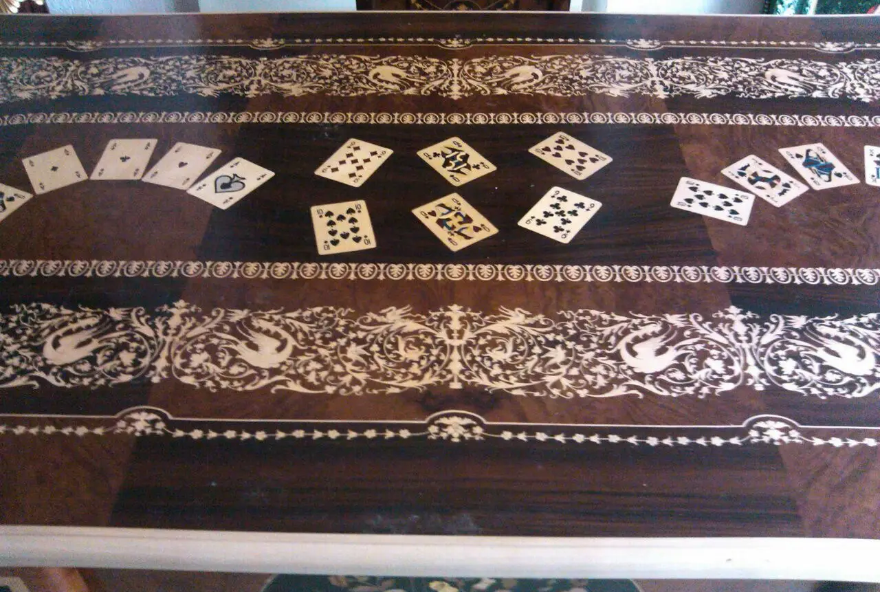 "Opera di Ay Mohsen realizzata con la tecnica dell'intarsio. Il titolo è Scrivania del poker e le tre carte e rientra nella categoria Ebanisteria Monumentale. Questa imponente scrivania monumentale rappresenta una delle opere più concettualmente audaci, raffinate e politicamente consapevoli di Aly Mohsen. In essa, la grande tradizione dell’ebanisteria artistica europea viene trasformata in strumento narrativo, simbolico e apertamente critico, dando vita a un’opera che trascende la funzione d’arredo per assumere la forma di messaggio cifrato e denuncia silenziosa. Non si tratta di un semplice mobile funzionale, ma di una vera opera d’arte tridimensionale, concepita per dialogare con il potere, smascherarne i meccanismi e mettere in crisi le apparenze di legalità e correttezza. Struttura e materiali La scrivania è caratterizzata da una struttura solida ma visivamente equilibrata, con gambe sagomate e slanciate che alleggeriscono la massa monumentale del piano. L’opera è realizzata con una selezione estremamente ricercata di legni pregiati, scelti non solo per le qualità estetiche ma anche per il loro valore simbolico: Noce nazionale e noce canaletto per la struttura principale e le superfici estese, apprezzati per la profondità cromatica e la stabilità nel tempo Radica di noce per i pannelli frontali, impiegata per ottenere superfici vibranti e irregolari, metafora visiva dell’instabilità e dell’inganno Ebano ed essenze scure tinte per i fondi degli intarsi, funzionali a rafforzare il contrasto grafico Acero e acero sicomoro per gli intarsi chiari Legni naturalmente colorati (padouk, acero, mogano, rovere, radica di noce, ebano verde ed ebano nero) per la resa cromatica delle figure e delle carte da gioco Il bordo chiaro e continuo del piano richiama deliberatamente la tradizione dei grandi tavoli da gioco, incorniciando la scena e convogliando lo sguardo verso il centro narrativo. Il piano: il gioco come metafora del potere Il piano superiore costituisce il cuore concettuale dell’opera. All’interno di una ricchissima cornice ornamentale intarsiata si sviluppa una sequenza di carte da poker disposte con apparente casualità. A una prima lettura, l’immagine suggerisce una partita in corso. A uno sguardo più attento, emerge però un elemento perturbante: le combinazioni non conducono a nessun esito logico. Le mani sono incoerenti, impossibili, volutamente manipolate. Questa ambiguità è intenzionale. Il poker, simbolo di strategia, calcolo e rischio controllato, viene qui messo in relazione con il gioco delle tre carte, archetipo universale della truffa. Il messaggio è sottile ma inequivocabile: chi crede di giocare secondo regole condivise è già vittima di un inganno. Il fronte: musica, scena e finzione Il fronte della scrivania è dominato da un grande medaglione circolare intarsiato, nel quale compaiono strumenti musicali, spartiti, carte da gioco e motivi floreali. La musica diventa metafora della messa in scena del potere: un concerto apparentemente armonioso che nasconde dissonanze profonde, una composizione elegante pensata per distrarre, sedurre e confondere. Le fasce laterali, ornate con ghirlande classiche e figure stilizzate, richiamano consapevolmente il linguaggio neoclassico e ottocentesco, rafforzando l’idea di ordine, autorità e rispettabilità — un ordine solo apparente. Storia dell’opera e valore simbolico La scrivania fu commissionata da un importante uomo d’affari egiziano, figura di enorme peso economico internazionale. Aly Mohsen, che conosceva il committente fin dall’infanzia, aveva fondati motivi per ritenere che questi operasse in realtà come prestanome per i servizi segreti statunitensi, coinvolto in operazioni economiche e finanziarie condotte in Italia. Al momento della consegna, Mohsen si recò personalmente nell’ufficio del committente e ne spiegò il significato con parole che rivelano la natura profonda dell’opera: «Questa scrivania serve per avvisare chi si siede di fronte a te: lui pensa di giocare a poker, mentre tu stai giocando al gioco delle tre carte.» Un’accusa di straordinaria eleganza, affidata non al linguaggio diretto ma alla forza simbolica dell’intarsio. Il committente, comprendendo perfettamente il messaggio, si sentì apertamente insultato e rifiutò l’opera. La scrivania rimase così nelle mani dell’artista. Rimasta nella disponibilità dell’artista, la Scrivania del Poker e del Gioco delle Tre Carte possiede oggi un valore ulteriormente accresciuto. È un pezzo unico, documentato, con una storia forte, verificabile e di straordinaria attrattiva per il collezionismo internazionale. L’opera unisce: alta ebanisteria artistica contenuto politico e narrativo qualità museale dimensioni monumentali provenienza diretta dall’artista Per collezionisti evoluti e investitori in mobili d’arte, arti decorative e opere concettuali, questa scrivania rappresenta un caso raro di arredo che diventa linguaggio critico, capace di dialogare con design, scultura e arte contemporanea, e destinato a una progressiva valorizzazione culturale e patrimoniale. In Aly Mohsen, il legno non è mai solo materia: diventa linguaggio, accusa, ironia e memoria. E questa scrivania ne è una delle dichiarazioni più lucide e implacabili."